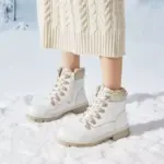 A person stands on snow wearing a cream knit skirt and white Wholesale Ankle Boots Snow Weather for Women Leather Zipper Casual Waterproof Winter Plush Boots.