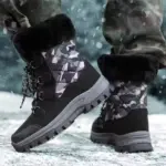 A person stands outdoors on snowy ground wearing Wholesale Black Mixed Anti-slip Women Snow Boots, large size TPR PU canvas, plush lining, and laced cotton design—these boots offer style and warmth for winter.