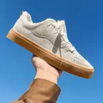 A hand holds up a pair of Customizable Retro Mixed Stylish Plush Walking Sneakers for women, featuring lightweight, breathable materials and a rubber sole, against a clear blue sky.