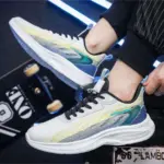 A person wearing Custom Wholesale Men Shoes Shock Rebound OEM Outdoor Running Sneakers with blue, green, and yellow accents sits by a skateboard under blue strip lights.