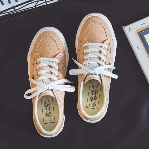 A pair of 2025 Customized Wholesale Retro Street Trending Women’s Solid Color Flat Canvas Sneakers, perfect for OEM/ODM orders, are placed side by side on a dark surface.