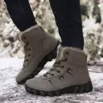 Someone wearing Customized Plush Laced Winter Snow Boots Anti Slippery Warm Waterproof Rubber PU Cotton Shoes and black pants stands outdoors on a snowy surface.