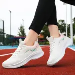 A woman stands on a red running track outdoors wearing 2024 Custom Mesh Sneakers Sport Women Running Shoes, featuring white with light blue and pink accents—fashionable, breathable sneakers for women and ladies.
