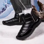 Person wears Wholesale New Fashion Outdoor Shiny Cotton TPR Snow Boots with side zippers, round toe, paired with white socks and dark pants, standing on snow.