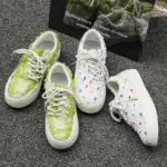 Two pairs of Bulk Zapatos De Hombre custom classic embroidery skateboarding canvas shoes—one green and frayed, one white with colorful dots—showcase unique OEM/ODM designs beside a reflective sign.