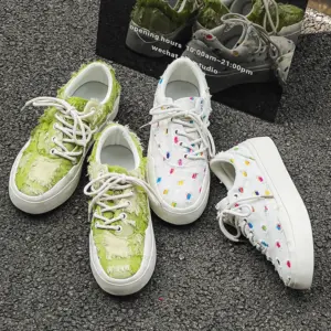 Two pairs of Bulk Zapatos De Hombre custom classic embroidery skateboarding canvas shoes—one green and frayed, one white with colorful dots—showcase unique OEM/ODM designs beside a reflective sign.