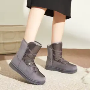 A person stands on a beige rug wearing the 2025 New Winter Round Toe Chunky Heel Leather Boots for Women—gray, mid-calf, waterproof, and platform with black laces; only their legs and boots are visible.