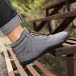 A person wearing Factory Wholesale Direct Sale Fashion Outdoor Men Women Snow Boots Cold Resistant Soft Cotton Shoes with black soles rests their foot on a rusty metal bench outdoors.