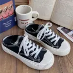 A pair of Breathable Designed Women Shoes Solid Cotton Sneakers Slip on Low Top Women Canvas Shoes with white laces are placed on a wooden surface beside an open book, a cup, and a closed book.