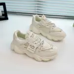 A pair of Women's Sneakers Low Top Mesh Thick Sole Height Increasing Wear Resistant Outdoor Sports Shoes, in white with side text details, are displayed on a white surface near a window.