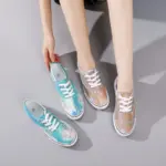 A person sits on the floor wearing one Wholesale China Factory Round Toe Unisex Canvas Tie Dye Shoe and holding another in a different color, both featuring white laces and soles.