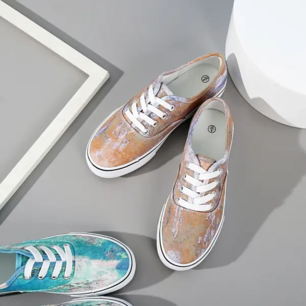 Two pairs of wholesale round toe unisex tie dye canvas shoes for women, featuring artistic pastel designs, are displayed on a gray surface beside white and gray geometric decor.