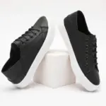 A pair of Fashion Low Top PU Upper Flat Black Walking Canvas Shoes for women with white soles shown on and beside a white cube against a plain background.