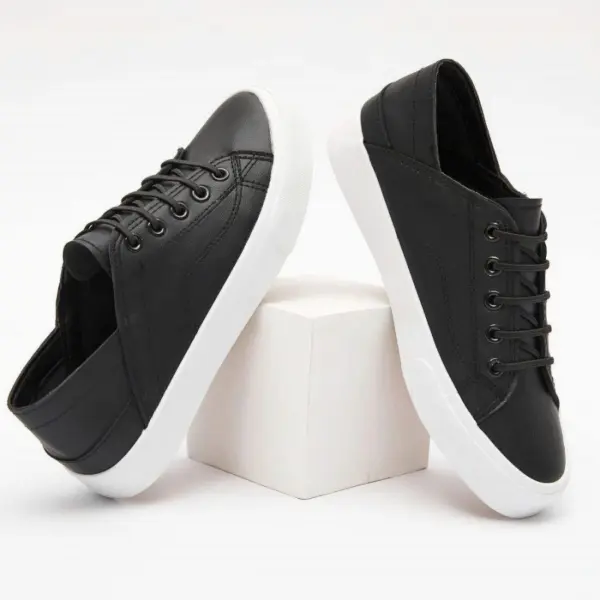 A pair of Fashion Low Top PU Upper Flat Black Walking Canvas Shoes for women with white soles shown on and beside a white cube against a plain background.