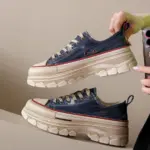 A person holds a pair of Women’s Casual Walking Style Canvas Chunky Shoes featuring blue denim uppers, cream-colored soles, and red accents against a neutral background.
