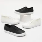 Four pairs of the Fashion Low Top PU Upper Casual Shoes—two black, two white—are displayed around a white rectangular block on a plain white background.