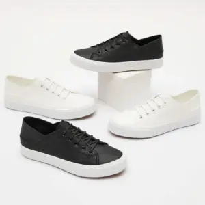 Four pairs of the Fashion Low Top PU Upper Casual Shoes—two black, two white—are displayed around a white rectangular block on a plain white background.
