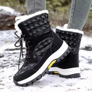 A person stands on a snowy surface wearing 2024 Customized LOGO Pattern Style Autumn Winter Trendi Warm Snow Boots with mixed PU and cotton, featuring black uppers, white soles, and faux fur lining.