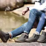 Two people sit outdoors on a rock with legs crossed at the ankles, wearing Factory Wholesale OEM ODM Low Top Waterproof Outdoor Cotton Snow Boots, ideal for large sizes and customization. Upper bodies are partially out of frame.