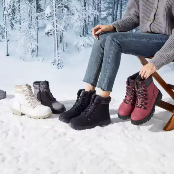 A person sits on a wooden chair in the snow, trying on four pairs of Wholesale Ankle Boots Snow Weather for Women and Men—leather, zipper, waterproof winter plush boots—in white, gray, black, and pink amid a snowy forest backdrop.
