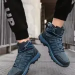 A person in blue Wholesale Customizable PU Warm Snow Boots Wear Resistant Anti-slip Hiking Shoes and black "UP" pants is jumping on a metal surface outdoors.