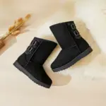 A pair of black Wholesale Fashion Western Designer Shoes Boot Fur Snow Women Winter Snow Boots for Women 2024 with two side buckles is displayed on a light surface beside a furry white rug and dried wheat stems.