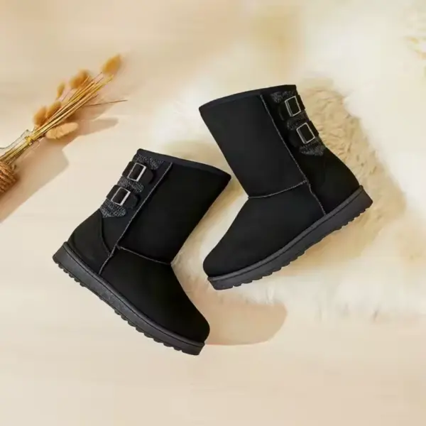A pair of black Wholesale Fashion Western Designer Shoes Boot Fur Snow Women Winter Snow Boots for Women 2024 with two side buckles is displayed on a light surface beside a furry white rug and dried wheat stems.