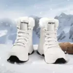 A pair of white OEM ODM winter waterproof anti-slip warm snow boots for women with fur lining and "OUTDOOR" on the tongue, shown on snowy ground with mountains—factory direct solid PU cotton shoes, customizable.
