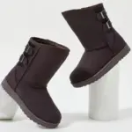 A pair of Wholesale Custom Designer Winter Snow Boots for women with side buckles, shown on white cylindrical stands against a plain background.