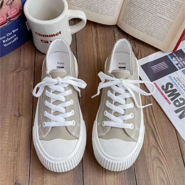 A pair of beige Breathable Designed Women Shoes Solid Cotton Sneakers Slip on Low Top Women Canvas Shoes are placed on a wooden surface beside an open book, a mug, and newspapers.