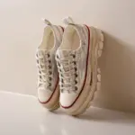 A pair of WomenS Casual Walking Style Canvas Shoes Chunky Shoes, featuring white uppers, textured soles, beige laces, and a subtle marble pattern, is positioned upright against a light-colored wall.