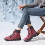 A person sits on a wooden chair in snowy outdoors, wearing blue jeans, a gray sweater, and Wholesale Ankle Boots Snow Weather for Women Leather Zipper Casual Waterproof Winter Plush Boots for Men. Snow-covered trees are visible in the background.