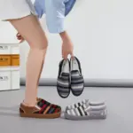 A person bends down, holding a pair of Fashion Ladies Comfortable Low Tops Stripe Printed Canvas Shoes, with two more pairs of these trendy stripe printed women's canvas shoes on the floor nearby.