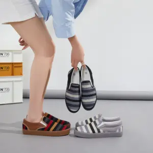 A person bends down, holding a pair of Fashion Ladies Comfortable Low Tops Stripe Printed Canvas Shoes, with two more pairs of these trendy stripe printed women's canvas shoes on the floor nearby.