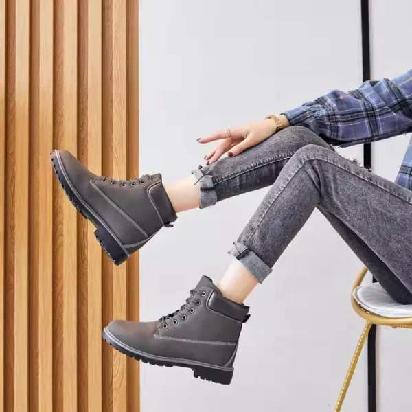 A person sits on a chair with legs crossed, wearing rolled-up jeans, a plaid shirt, and Women Snow High Top Mountain Climbing Ankle Boots—outdoor leather anti-slip ankle boots for women—against a light background with wooden paneling.