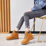 A person sits on a chair wearing rolled-up jeans, a blue plaid shirt, and Women Snow High Top Mountain Climbing Ankle Boots Anti-slip Outdoor Leather Boots for Women.