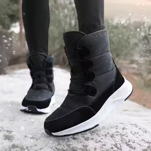 A person wearing Wholesale Wear Resistant Outdoor Cotton Snow Boots PU High Top Round Toe Rubber Women's Shoes with white soles stands on a snowy surface, trees visible in the background.