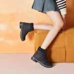 A person wears 2025 Winter Snow Ankle Boots for Men Women High Heel Platform Boots for Ladies, sitting on a mustard yellow cushioned seat with an orange background—perfect for stylish OEM ODM fashion collections.
