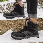 A person in Factory Warm Anti slip Breathable Snow Boots, wear-resistant rubber winter lace-up men's shoes, with fur lining, stands on snow-covered ground and rocks.