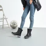 A person in blue jeans and black Wholesales Warm Snow OEM Custom Ankle Snow Leather Boots Furry Boots for Women stands near a folding chair and reflective sphere, highlighting the versatility of these women's fur boots in a minimal indoor setting.