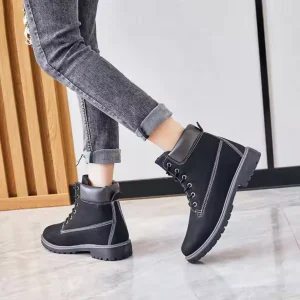 A person in cuffed gray jeans and Women Snow High Top Mountain Climbing Ankle Boots Anti-slip Boots Outdoor Leather Boots for Women stands indoors on a light tiled floor.