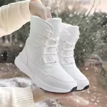 A person holds a pair of white Wholesale Wear Resistant Outdoor Cotton Snow Boots PU High Top Round Toe Rubber Women's Shoes with thick soles and lace-up fronts outdoors in the snow.