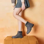 A woman in a denim skirt and striped sweater poses on a yellow stool, showing off stylish 2025 Winter Snow Ankle Boots for Men Women High Heel Platform Boots for Ladies Wholesale.